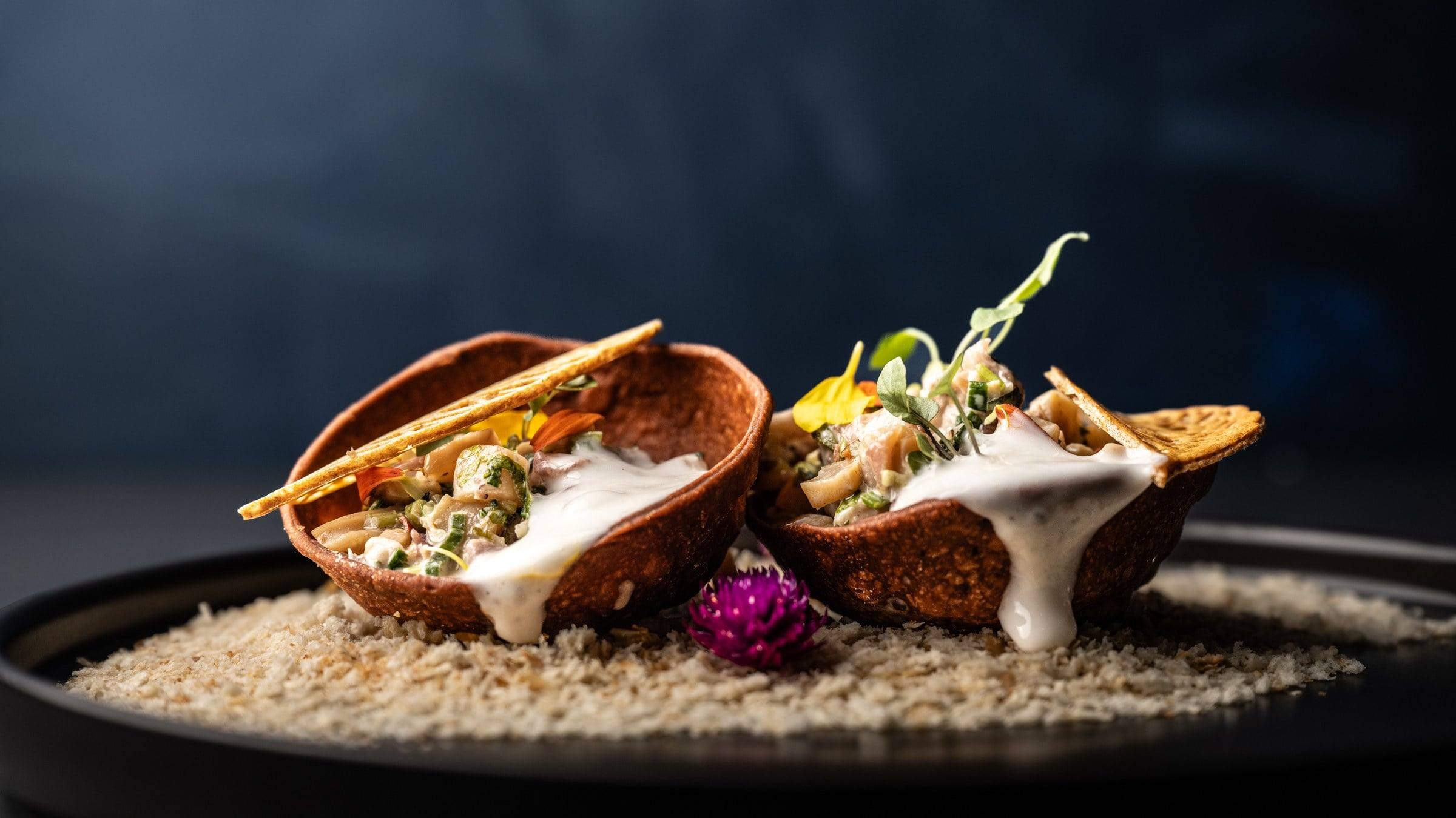 Ceviche servido en dos conchas crujientes sobre fondo azul oscuro