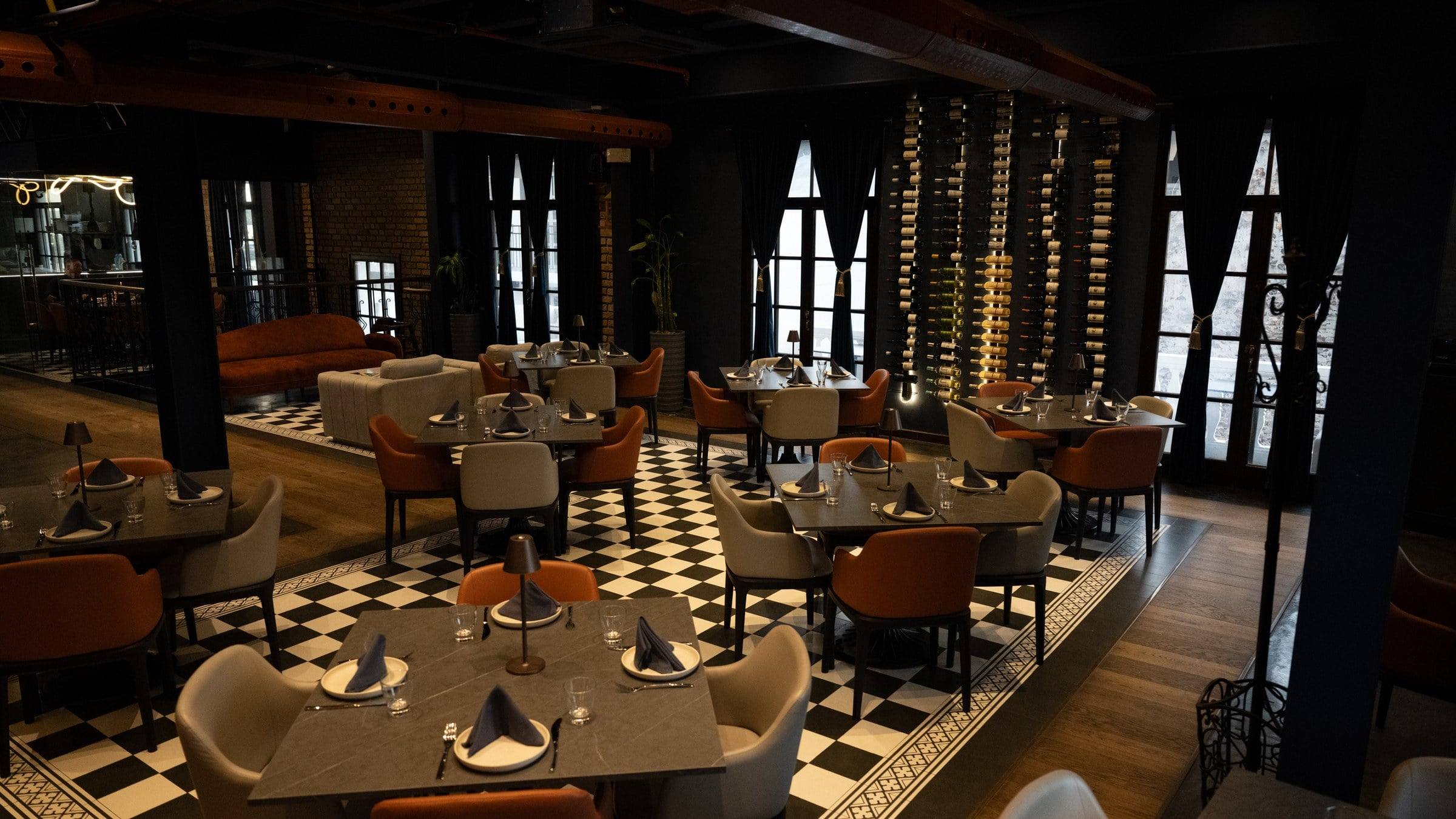 Salón de Marula con piso de damero blanco y negro, mesas montadas y una pared de botellas de vino